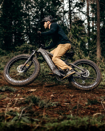 Mountainbiker mit schwarzem Helm fährt ein Himiway E-Mountainbike durch einen ruhigen Waldweg, Sonnenstrahlen fallen durch die hohen Bäume auf den Waldboden